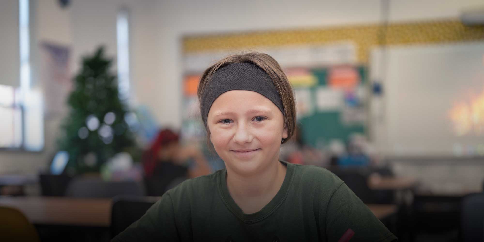 Smiling student wearing a headband in a classroom.
