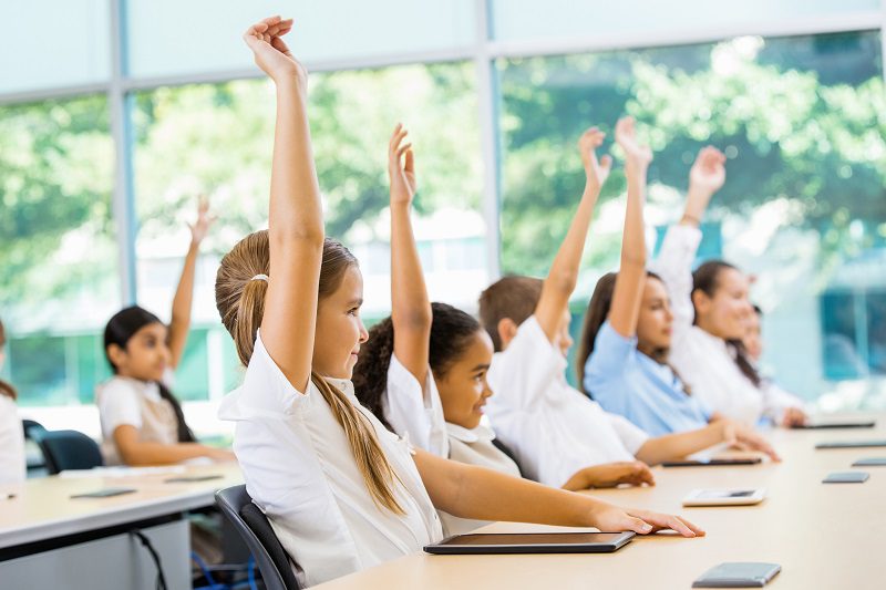 Students sitting at a desk with hands raised.